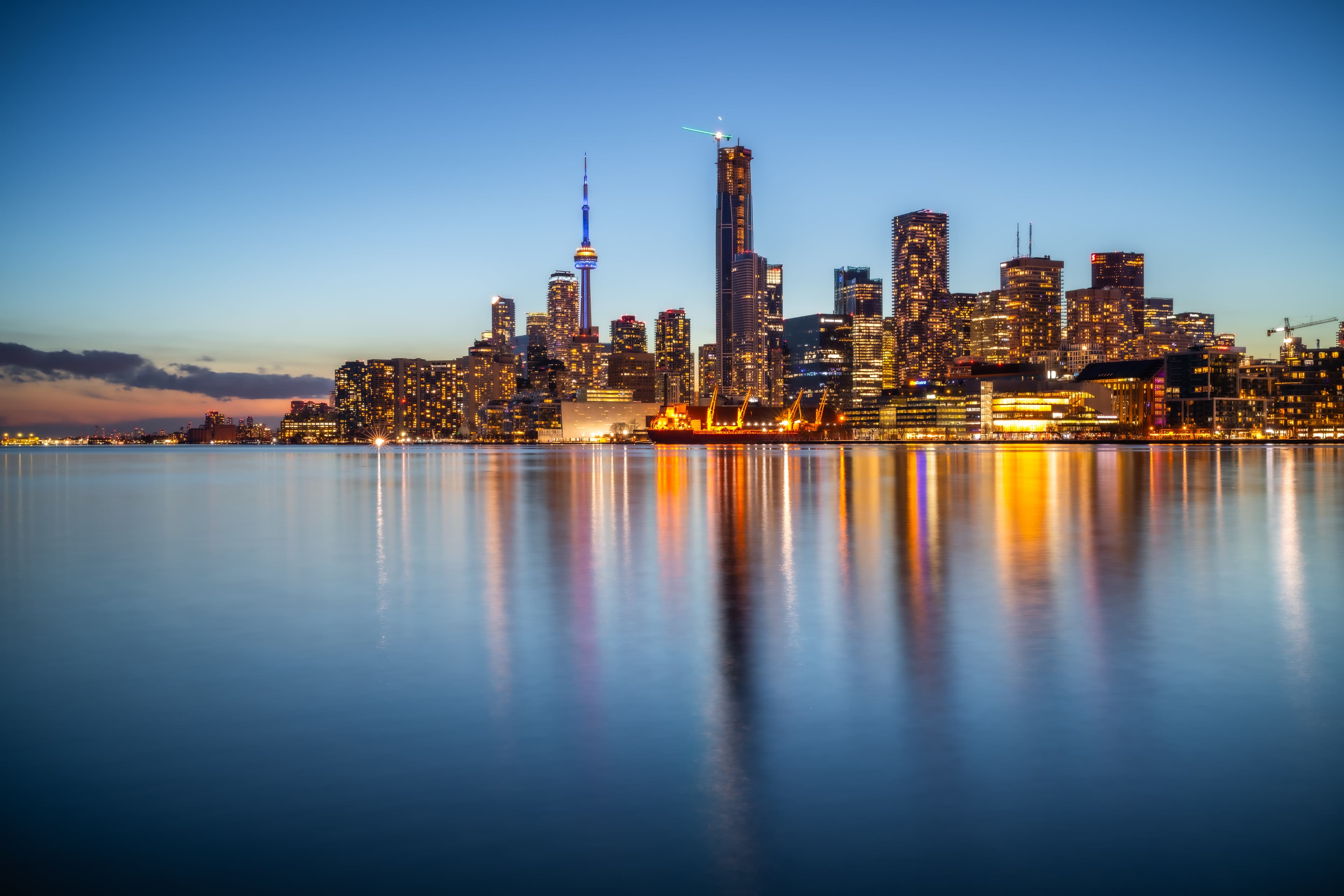 Toronto skyline at dusk reflected over calm water.