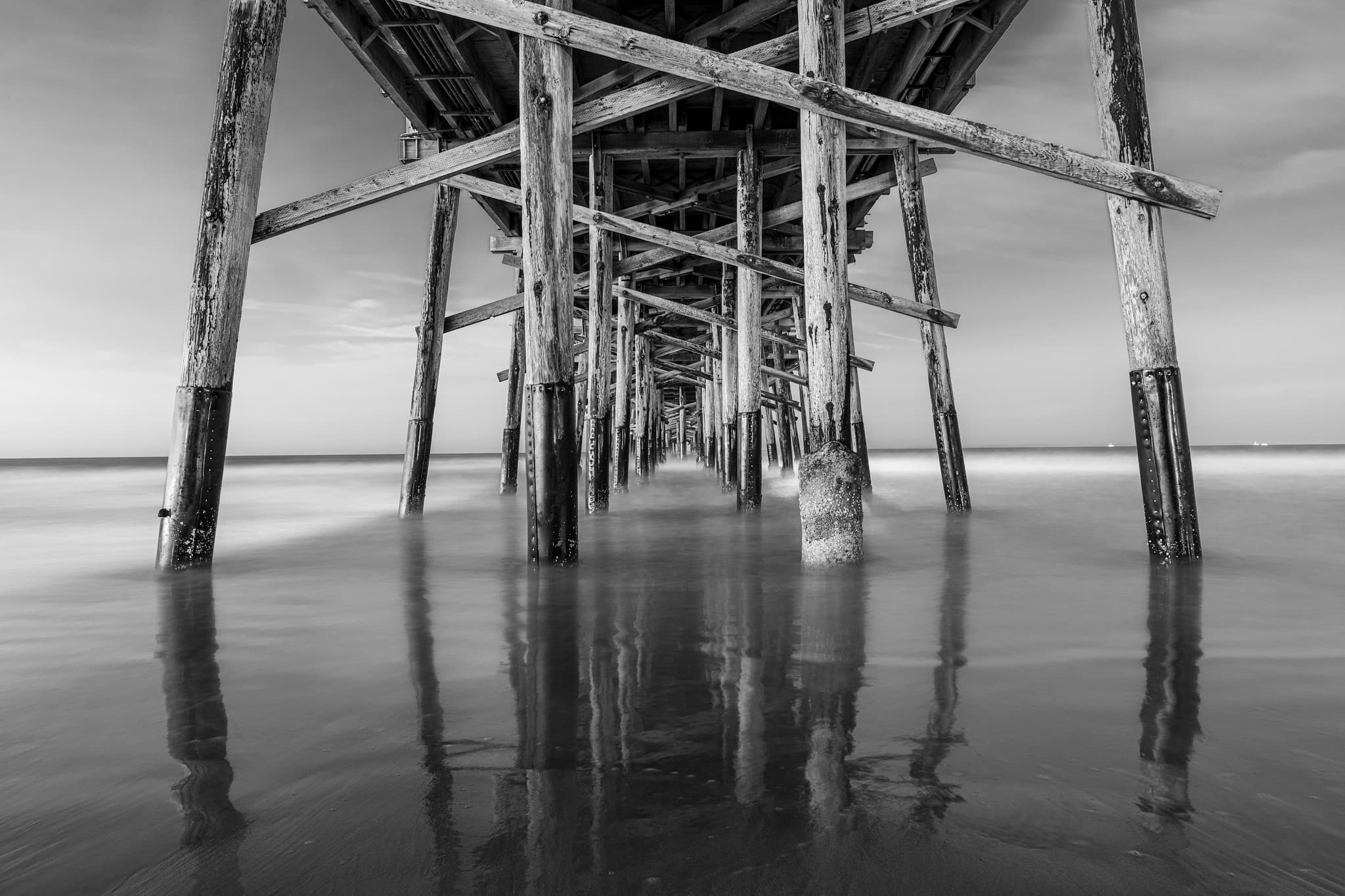 Black and white photograph beneath a wooden pier.